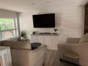 Una sala de estar con un televisor de pantalla plana montado en la pared, un sofá, una mesa de centro y una mesita auxiliar.