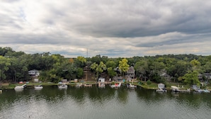 A lakeside view with boats docked, a dock, and houses surrounded by trees.