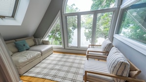 A cozy room with a sofa and a chair facing a large window, a plaid rug, and wooden flooring.