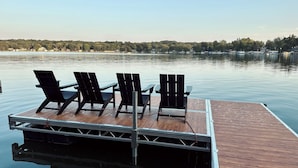 A wooden dock with four black chairs and a metal railing.