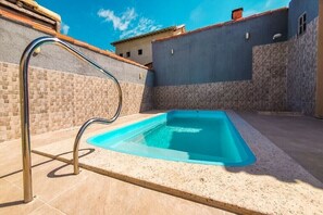 A swimming pool with a metal ladder, surrounded by a tiled patio and a stone wall.