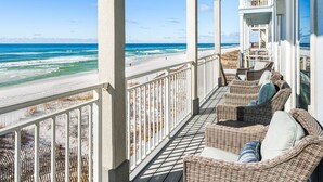 Een balkon met rieten meubilair met uitzicht op een strand.