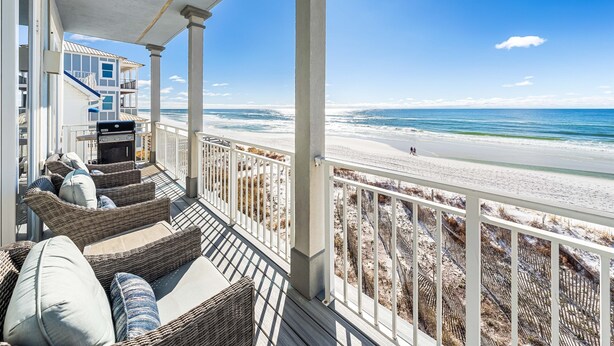 Een balkon met rieten meubilair met uitzicht op een strand.
