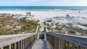Une promenade en bois menant à une plage où se trouvent une petite construction et un poste de surveillance pour les sauveteurs.