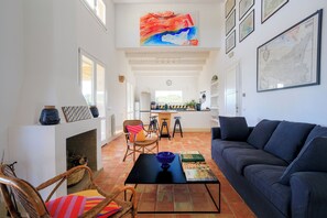 A spacious living room with a fireplace, a blue sofa, and a dining area in the background. - Baglio di Verre (Menfi)