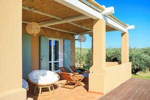 A covered outdoor seating area with wicker chairs and a cushioned bench, a wooden deck, and a view of greenery. - Baglio di Verre (Menfi)