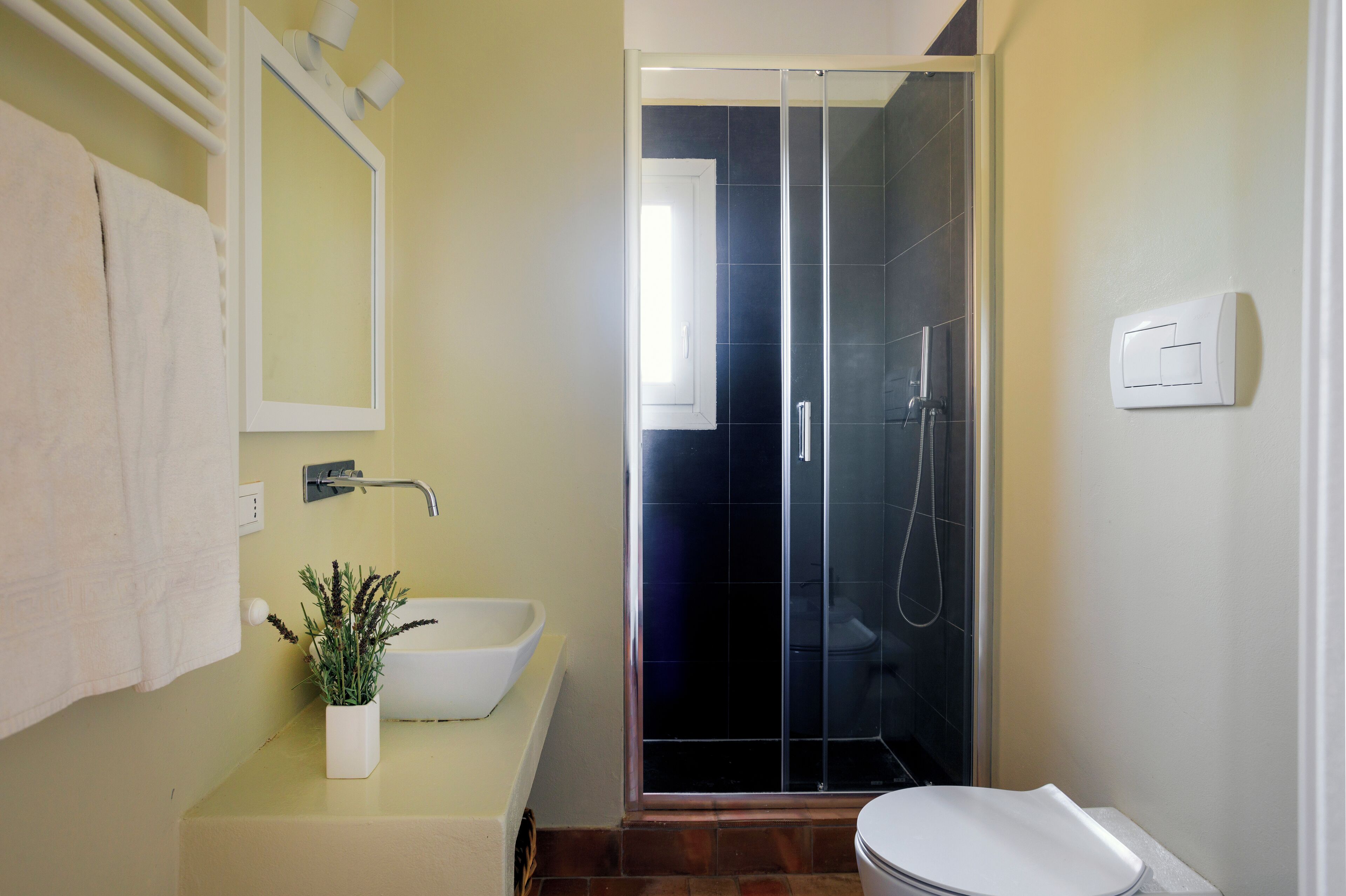 A bathroom with a white sink, a mirror, a potted plant, and a glass-enclosed shower.