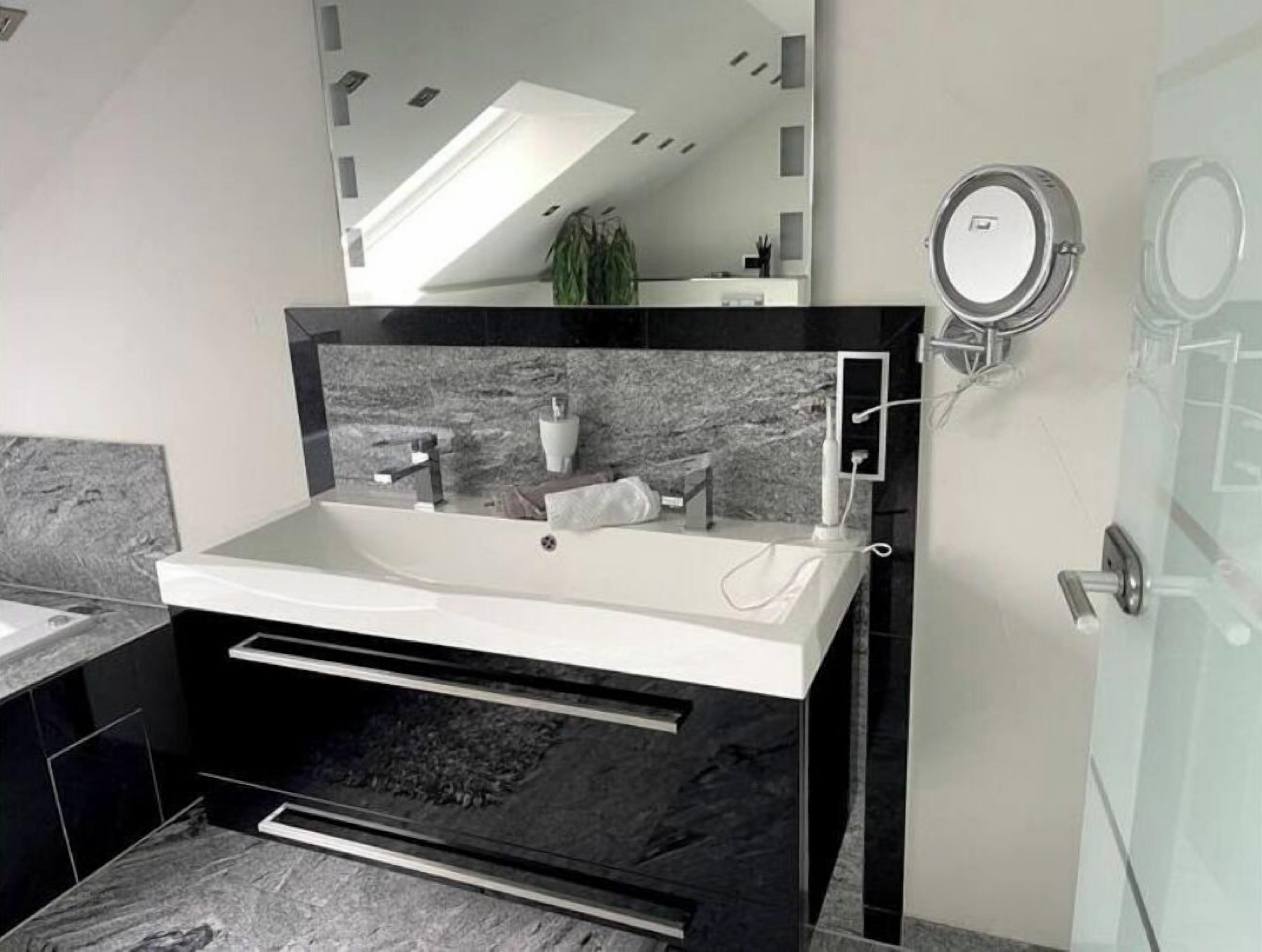 A modern bathroom with a large mirror, a sink, and a shower area.