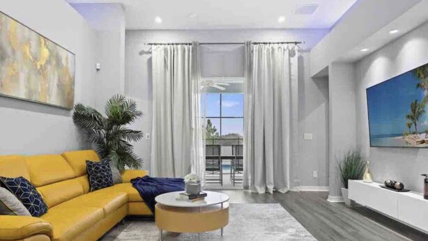 Uma sala de estar moderna com um sofá amarelo, uma mesa de centro redonda e uma janela grande com cortinas.