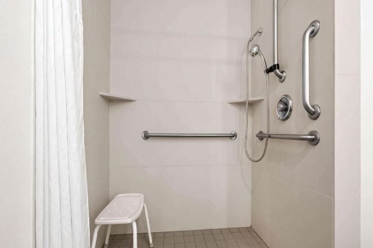 A bathroom with a white shower, grab bars, a white step stool, and a toilet.