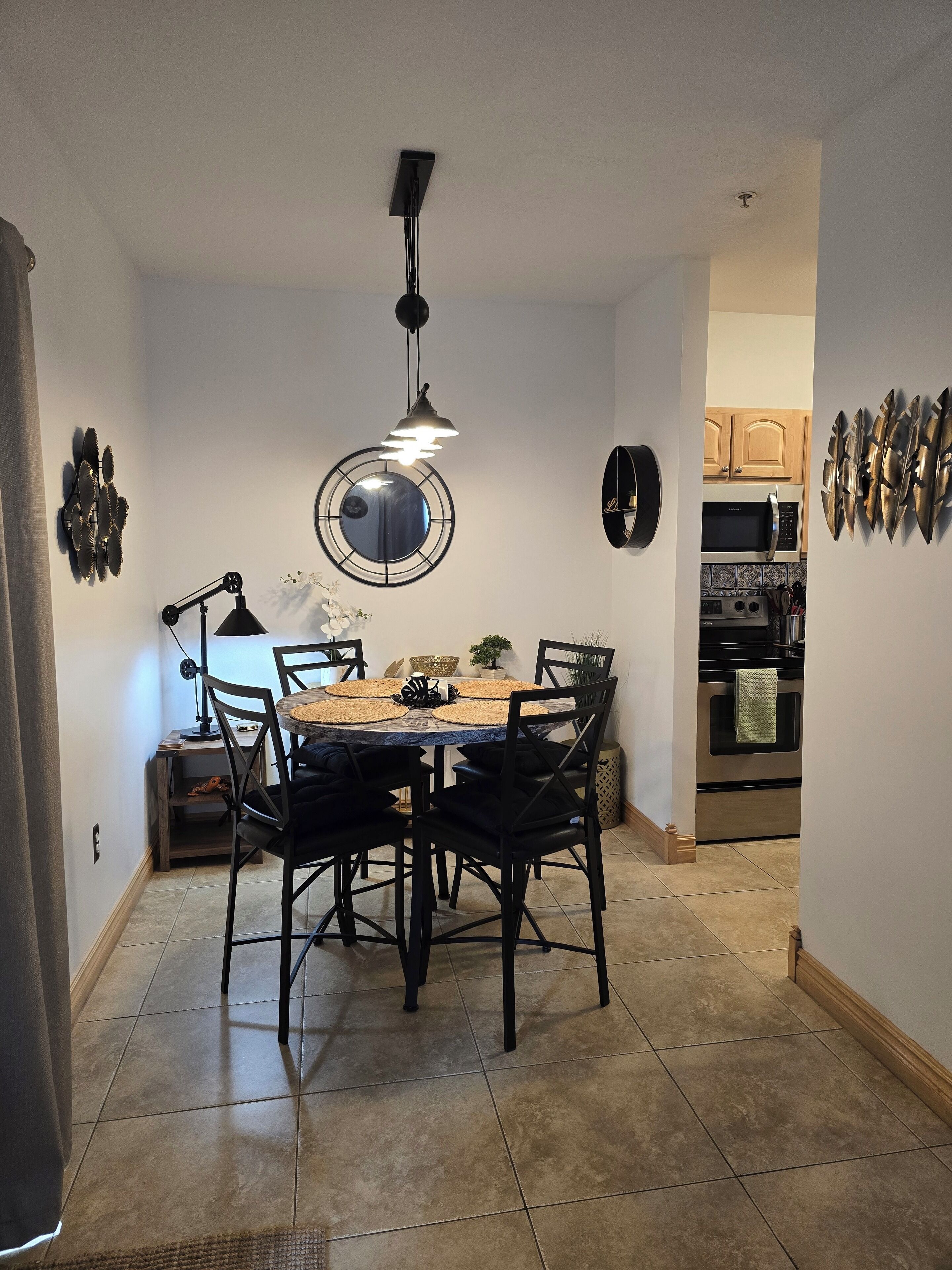 A dining area with a round table, black chairs, a pendant light, and a wall-mounted mirror.