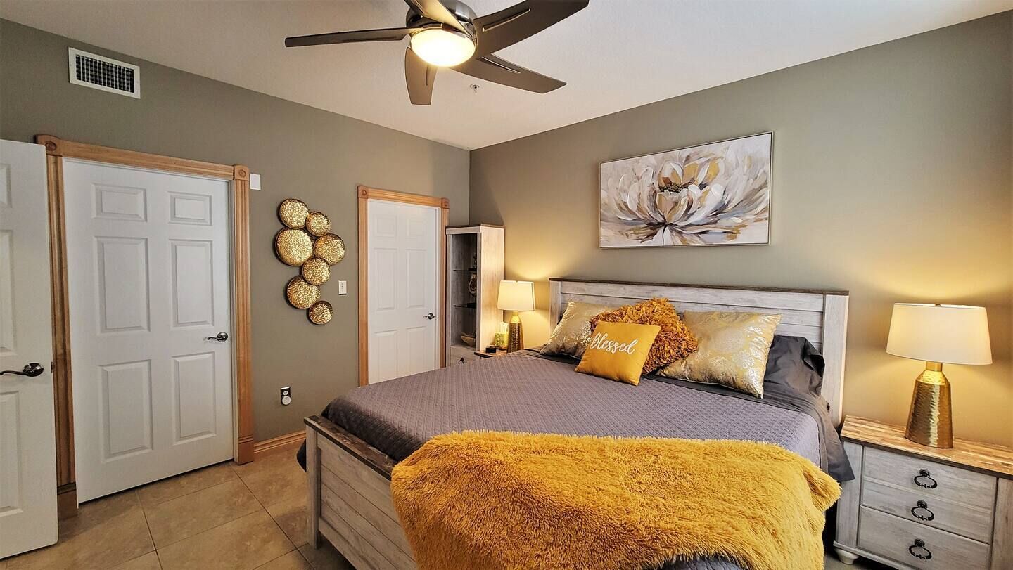 A bedroom with a bed, bedside lamps, a ceiling fan, and a wall-mounted artwork.
