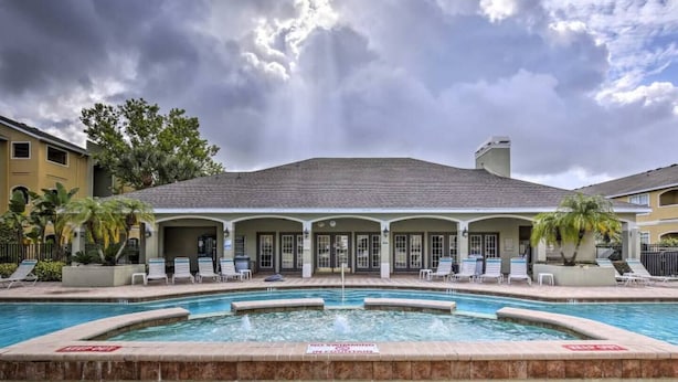 A pool area with lounge chairs, a fountain, and a building with a tiled roof. - Clearwater Condo w/Pool Access, 4Mi to Beach! (Clearwater)
