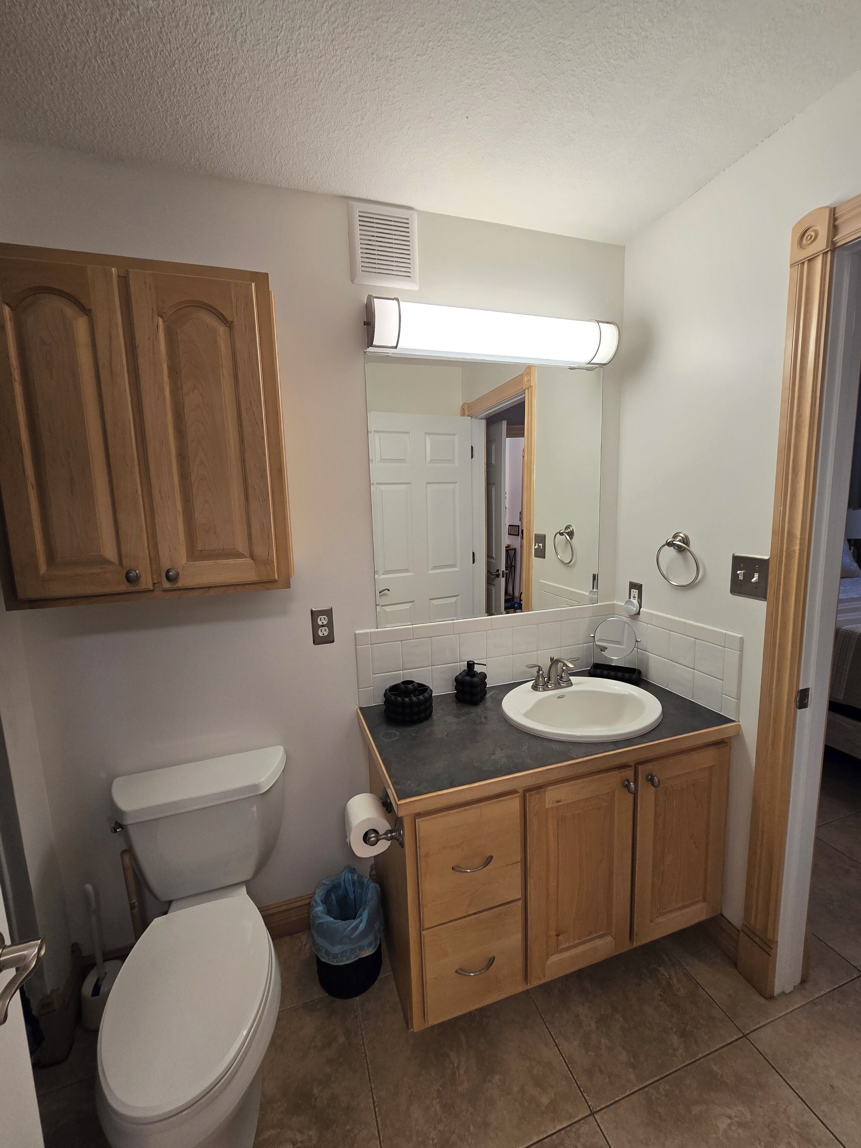 Une salle de bain comprenant des toilettes, un lavabo, des meubles en bois, un miroir et une poubelle.