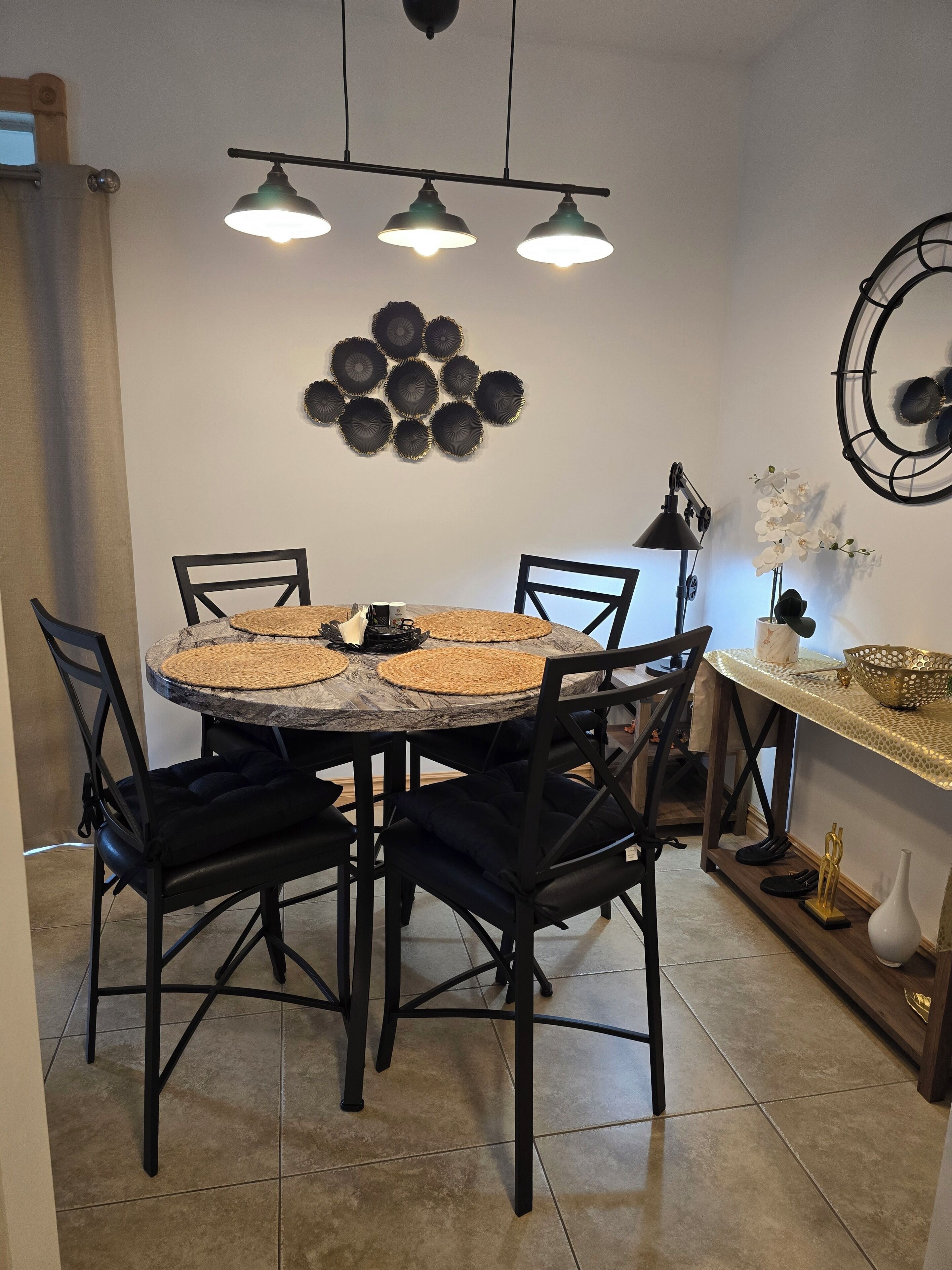 Un espace repas avec une table ronde, des chaises noires et un luminaire suspendu au plafond.