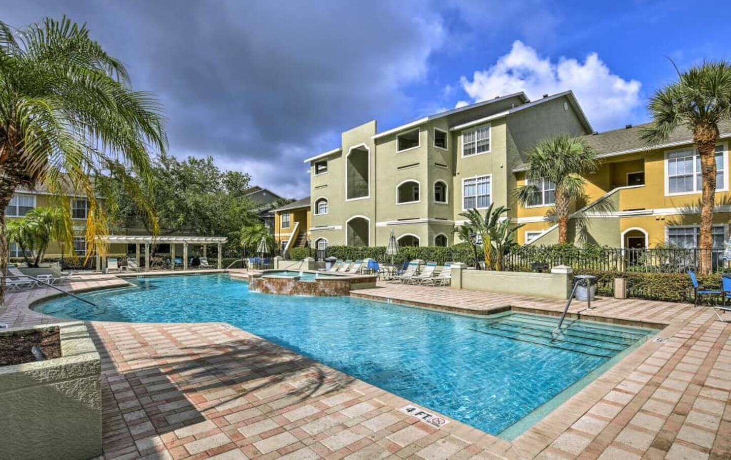 A swimming pool area with lounge chairs and a building with multiple balconies in the background.