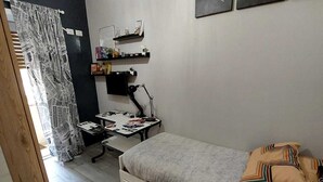 A bedroom with a bed, a desk, a chair, a world map on the wall, and a curtain with newspaper print. - Roman Holidays (Roma)