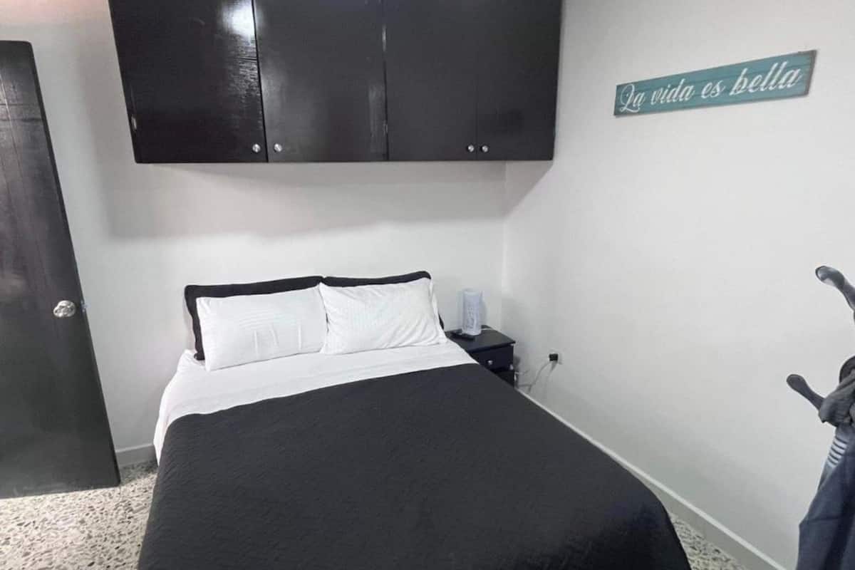 A bedroom with a bed, a dark wardrobe, a nightstand, and a wall sign.