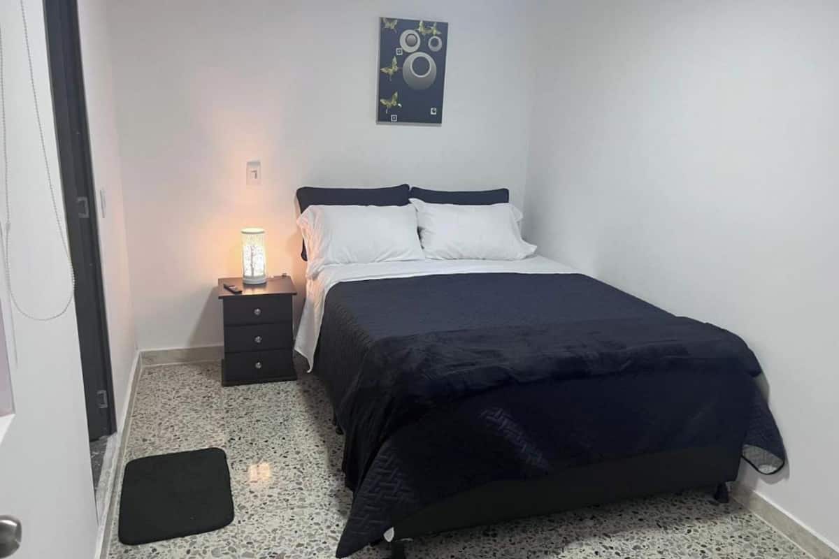 A bedroom with a bed, a nightstand, a lamp, and a wall art piece.