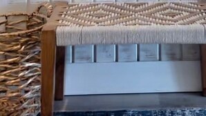 Una panca di legno con seduta in vimini, un cesto intrecciato e un cappello appeso al muro.
