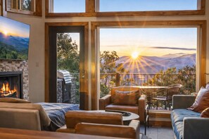 A room with a fireplace, a balcony with a view of the mountains, and a dining area with outdoor furniture.