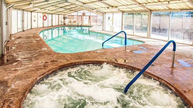 Een binnenzwembad met een jacuzzi, omringd door een overdekt terras met zitplaatsen.