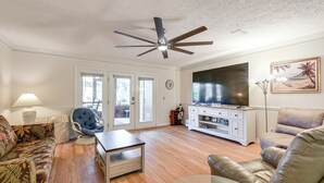 Ein Wohnzimmer mit Deckenventilator, Fernseher, Sofa, Couchtisch und Sessel.