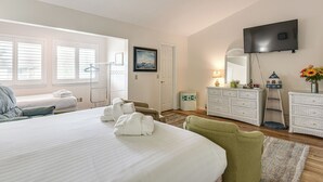 Ein Hotelzimmer mit einem großen Bett, einem an der Wand befestigten Fernseher, einem Schminktisch und einem Sessel.