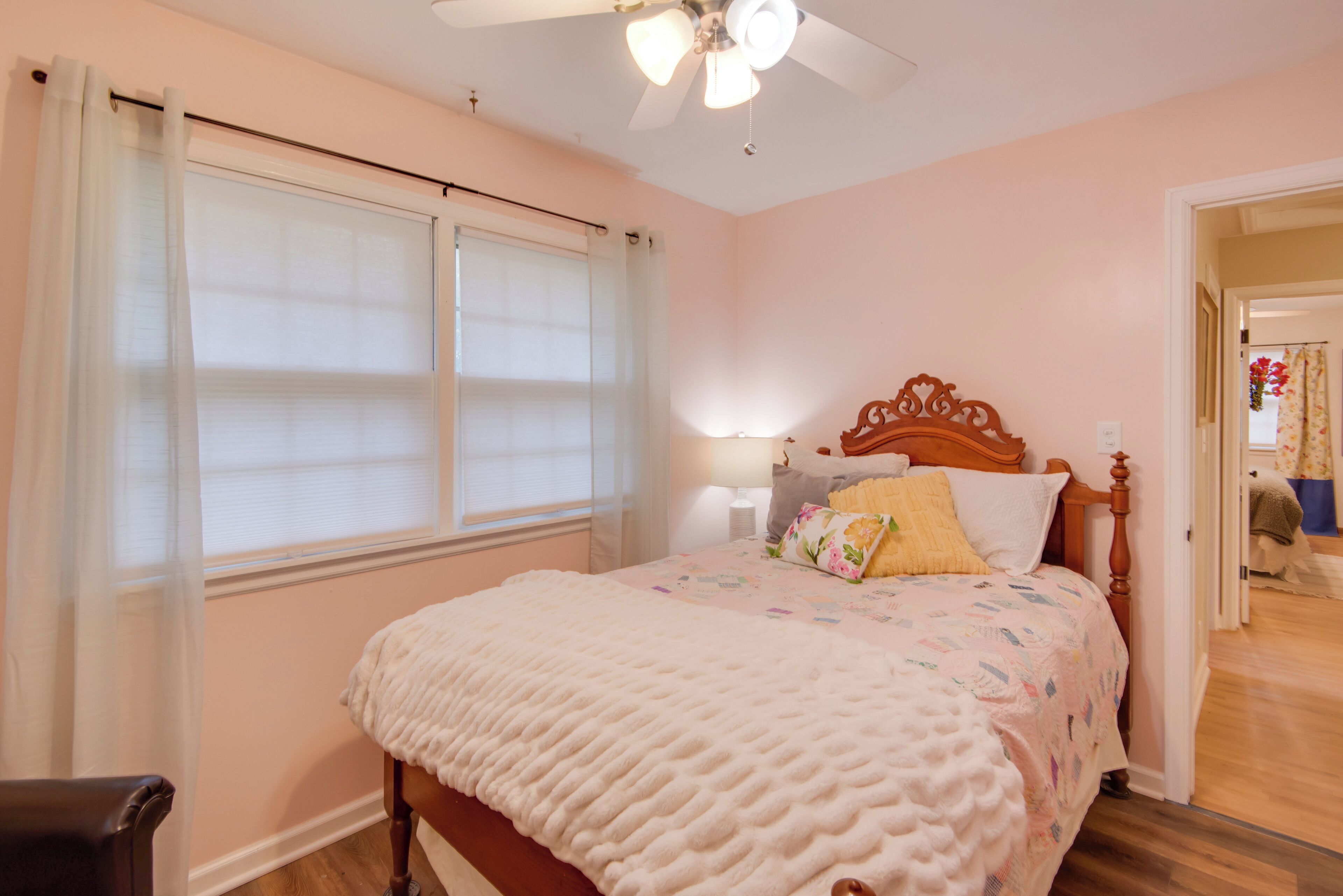 A bedroom with a bed, a ceiling fan, a window with curtains, and a nightstand with a lamp.