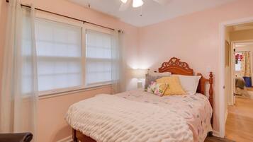 A bedroom with a bed, a ceiling fan, a window with curtains, and a nightstand with a lamp.