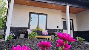 A modern house with a covered porch, a large window, and a garden with pink flowers. - Posh Pelican House is guest favorite in quaint resort town of Breezy Point! (Breezy Point)
