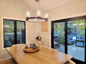A dining area with a wooden table, a chandelier, and a view of the outdoor patio with a grill and seating.