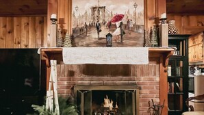 A fireplace with a mantel decorated with a painting, a white cloth, and a small Christmas tree. - Fun on the River - Swim, Fish, Hike Near Tubing (Blue Ridge)