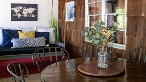A wooden dining table with a clear glass vase containing dried flowers, surrounded by metal chairs. A wooden bench with patterned cushions is visible in the background. - Fun on the River - Swim, Fish, Hike Near Tubing (Blue Ridge)