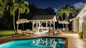 A swimming pool with lounge chairs and umbrellas, a barbecue area, and palm trees. - Luxe Golden Hour - Private Pool & Pickleball Court, Outdoor Kitchen (Palm Beach Gardens)