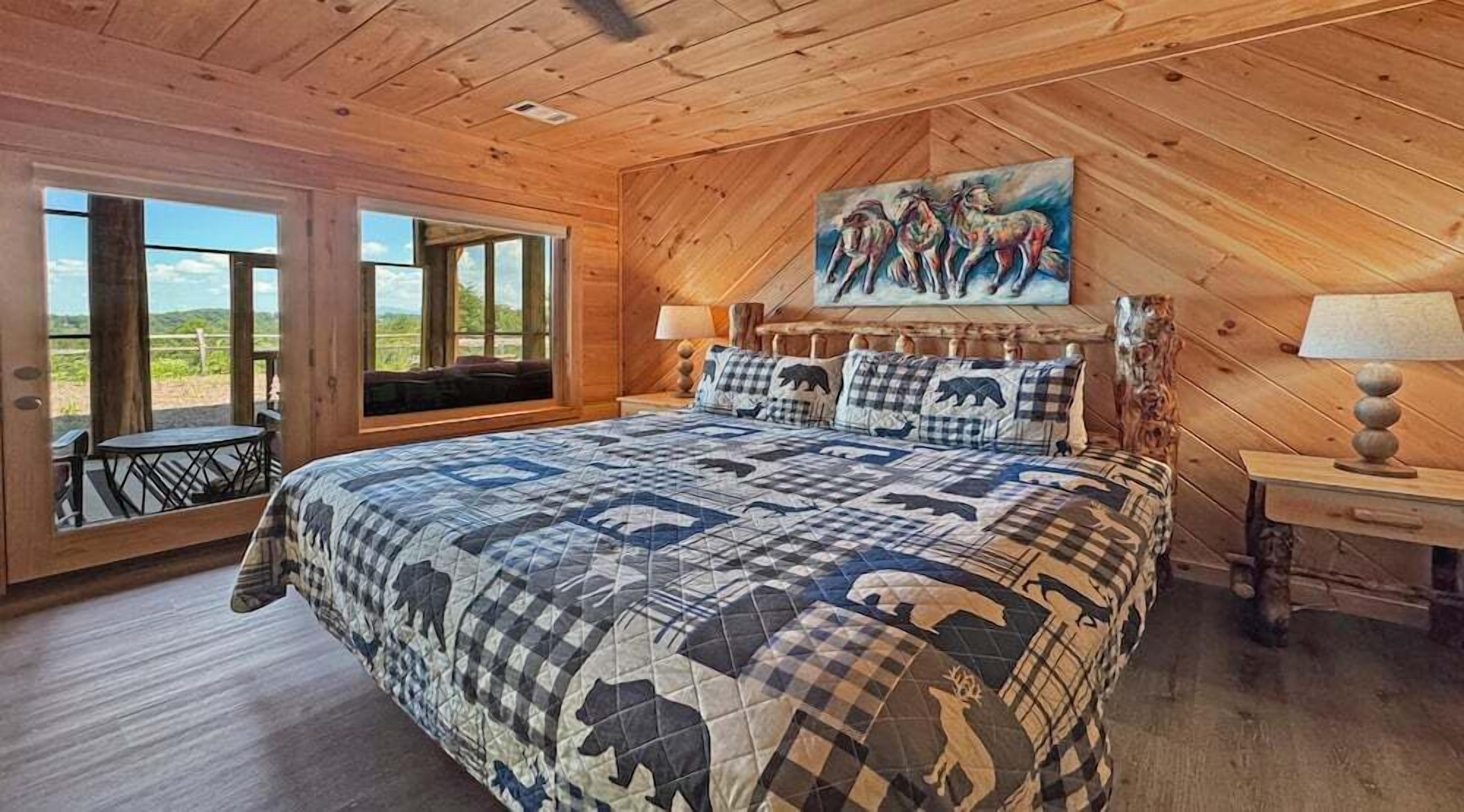 Une chambre à coucher avec un grand lit, un tableau représentant des chevaux, une fenêtre donnant sur un beau paysage et un plafond en bois.
