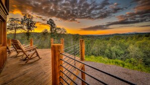 Een houten terras met ligstoelen met uitzicht op een bebost landschap tijdens de zonsondergang.