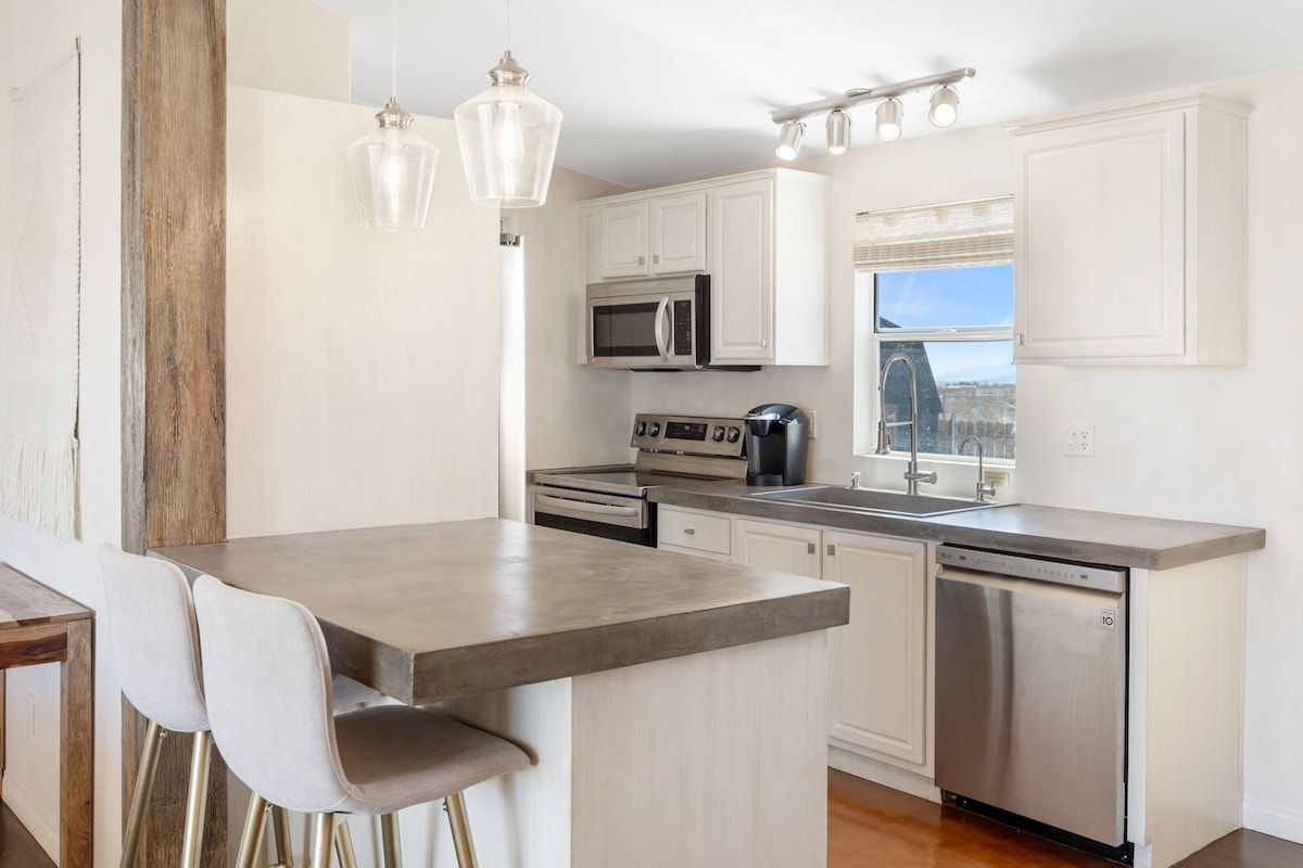 A modern kitchen with white cabinets, stainless steel appliances, and a bar area with stools.