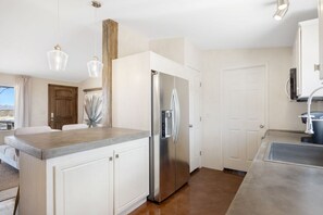 A modern kitchen with white cabinetry, a stainless steel refrigerator, and pendant lighting. - Desert Moon-Hot Tub & Views Near Joshua Tree! (Joshua Tree)