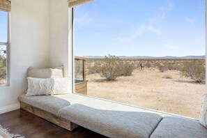 A room with a built-in bench seating area, a large window offering a view of a desert landscape. - Desert Moon-Hot Tub & Views Near Joshua Tree! (Joshua Tree)