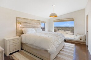 A bedroom with a large bed, bedside tables, a window with a view, and a hanging light fixture. - Desert Moon-Hot Tub & Views Near Joshua Tree! (Joshua Tree)