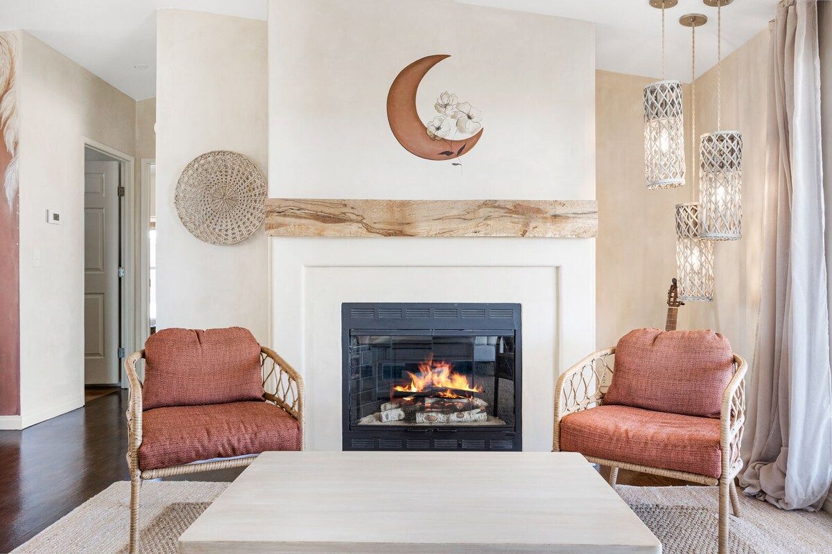 Een woonkamer met een open haard, twee rieten fauteuils, een salontafel en decoratieve wandkunst.