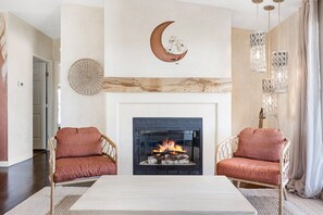 A living room with a fireplace, two wicker chairs, a coffee table, and decorative wall art.