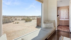 Quarto com uma grande janela, um sofá e vista para paisagem desértica.