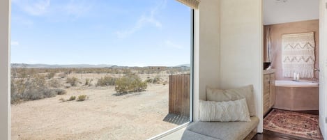 A room with a large window, a sofa, and a view of a desert landscape.