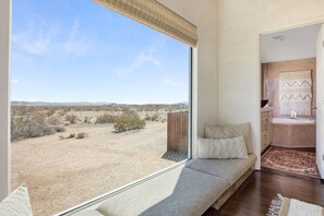 A room with a large window, a sofa, and a view of a desert landscape. - Desert Moon-Hot Tub & Views Near Joshua Tree! (Joshua Tree)