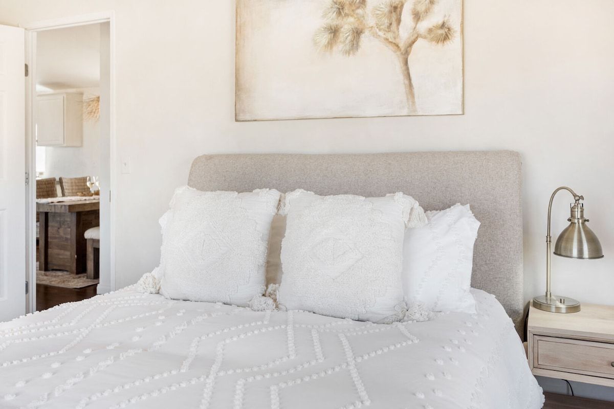 A bedroom with a bed, pillows, a nightstand, a lamp, and a framed picture on the wall.