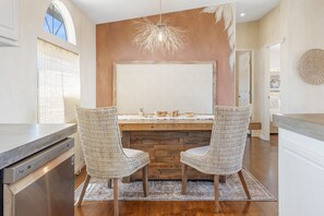 A kitchen with two wicker chairs, a wooden island, and a hanging light fixture. - Desert Moon-Hot Tub & Views Near Joshua Tree! (Joshua Tree)