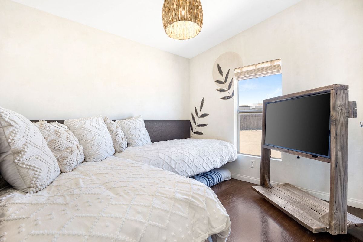 A bedroom with a bed, a television on a wooden stand, and a window with a view.