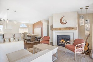 A spacious living room with a fireplace, comfortable seating, and a dining area. - Desert Moon-Hot Tub & Views Near Joshua Tree! (Joshua Tree)